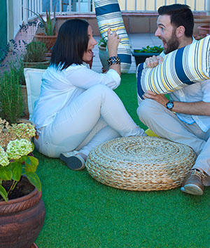 Young couple dressed in white clothes getting the terrace ready to enjoy Valentine's day at home, using plants, turf, and cushions